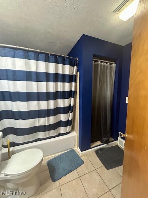 bathroom with tile patterned floors, shower / bath combo with shower curtain, a textured ceiling, and toilet