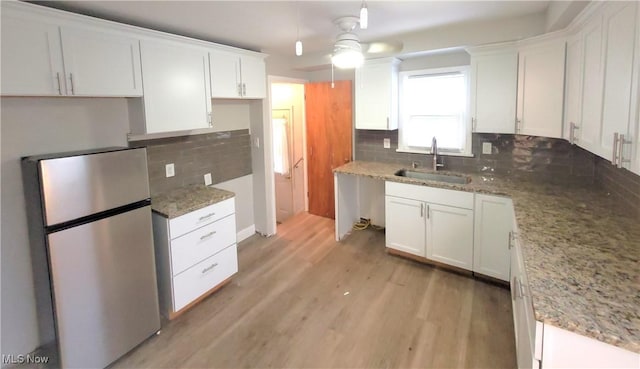 kitchen with white cabinetry, sink, light stone counters, stainless steel fridge, and decorative backsplash