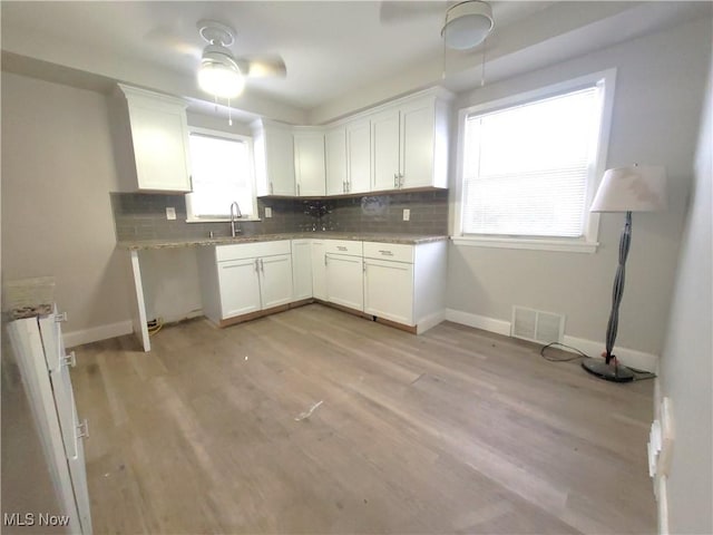 kitchen featuring light stone countertops, white cabinetry, sink, and light hardwood / wood-style flooring