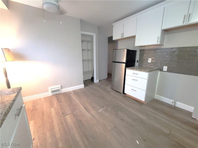 kitchen with backsplash, stainless steel fridge, light hardwood / wood-style flooring, and white cabinets