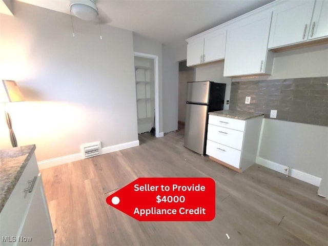 kitchen with stainless steel refrigerator, white cabinetry, backsplash, light stone countertops, and light wood-type flooring