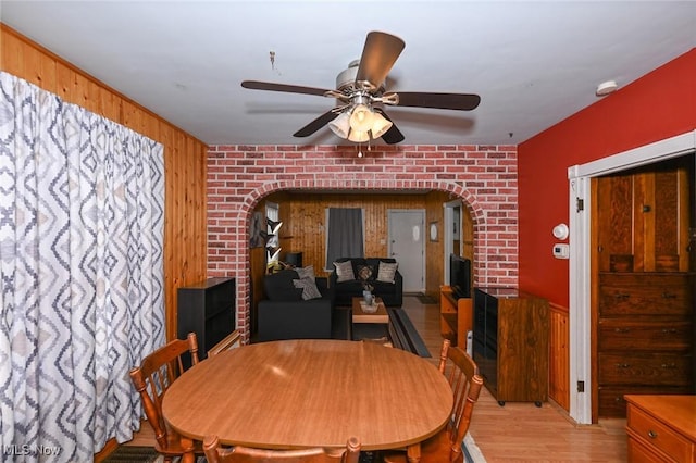 dining area featuring wooden walls, ceiling fan, brick wall, and light hardwood / wood-style flooring