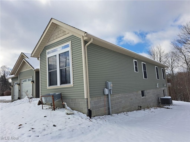 view of snow covered exterior with a garage and central air condition unit