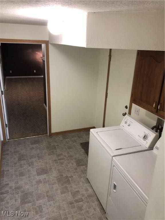 clothes washing area with washing machine and clothes dryer, light carpet, cabinets, and a textured ceiling