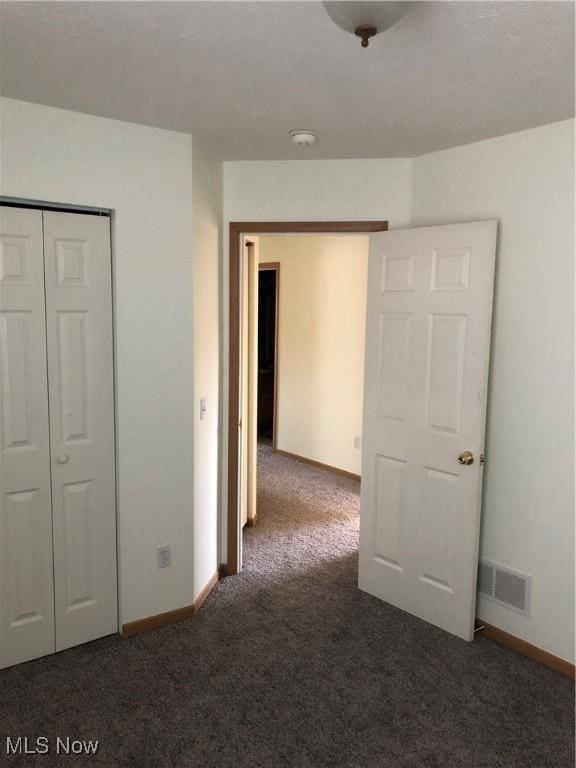 unfurnished bedroom with a closet and dark colored carpet