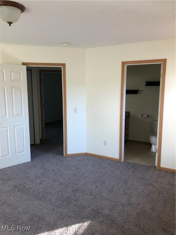 unfurnished bedroom featuring dark carpet, a spacious closet, and connected bathroom