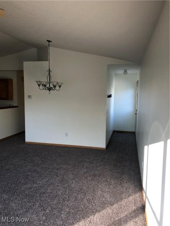 empty room with a chandelier, dark colored carpet, and lofted ceiling