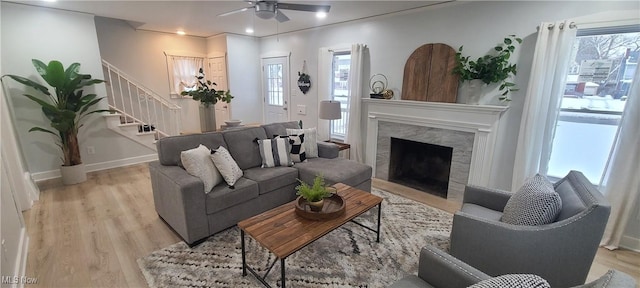 living room featuring a wealth of natural light, light hardwood / wood-style flooring, ceiling fan, and a premium fireplace