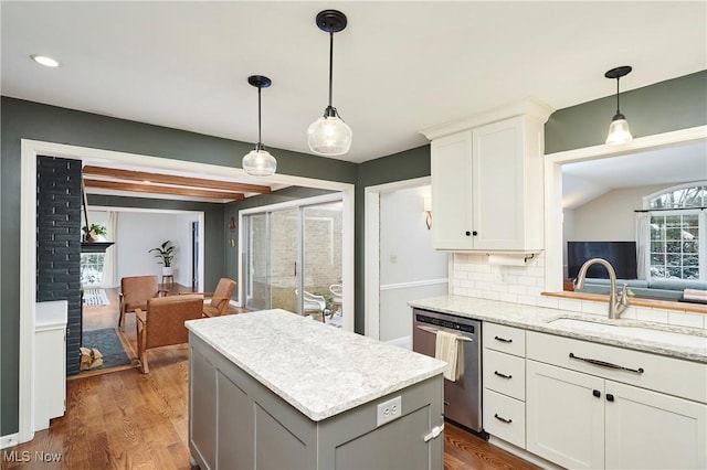 kitchen featuring backsplash, light stone counters, stainless steel dishwasher, sink, and white cabinetry