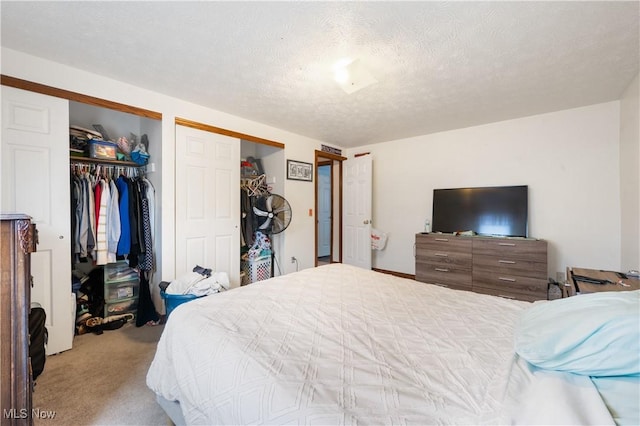 bedroom featuring a textured ceiling, light carpet, and multiple closets