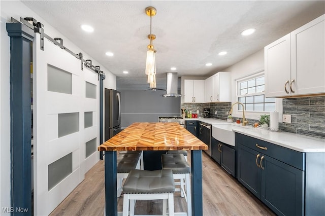 kitchen featuring blue cabinetry, sink, wall chimney exhaust hood, a barn door, and white cabinets