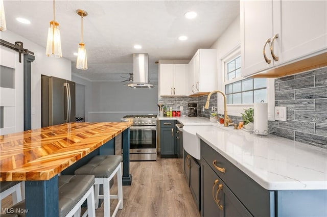 kitchen with white cabinetry, hanging light fixtures, stainless steel appliances, a barn door, and ventilation hood