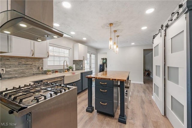 kitchen featuring white cabinetry, a barn door, blue cabinets, island exhaust hood, and pendant lighting