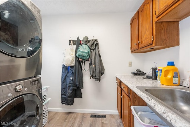 laundry area featuring sink, cabinets, light hardwood / wood-style flooring, stacked washer and dryer, and a textured ceiling