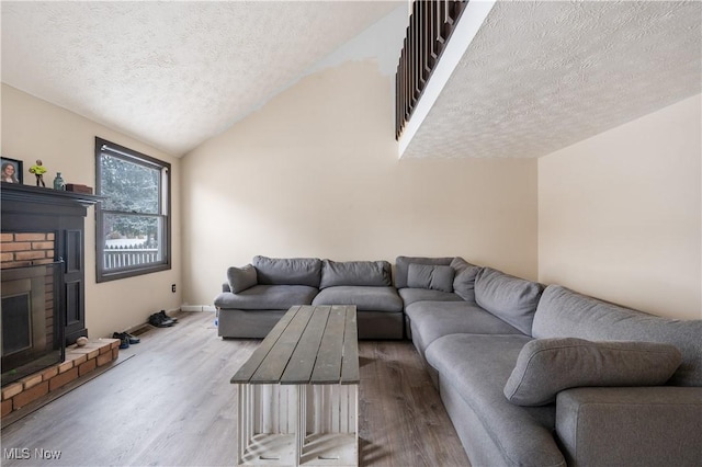 living room with hardwood / wood-style floors, a textured ceiling, a brick fireplace, and lofted ceiling