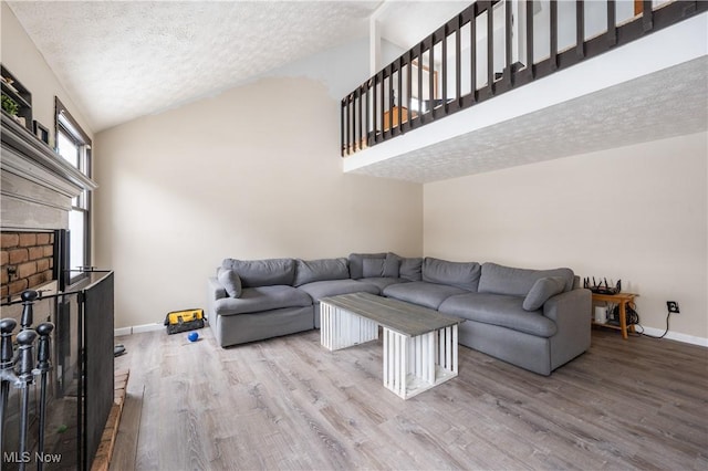 living room featuring hardwood / wood-style floors, a fireplace, a textured ceiling, and high vaulted ceiling