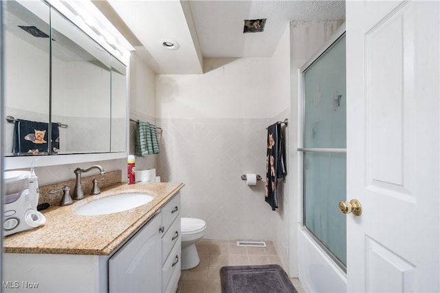 full bathroom with tile patterned floors, vanity, tile walls, enclosed tub / shower combo, and toilet