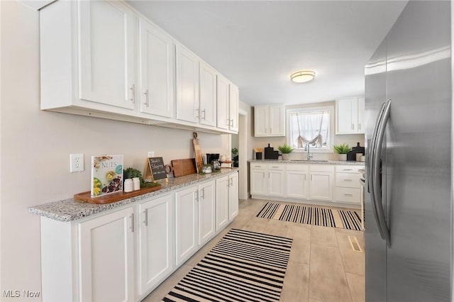 kitchen with stainless steel refrigerator, light stone countertops, and white cabinets