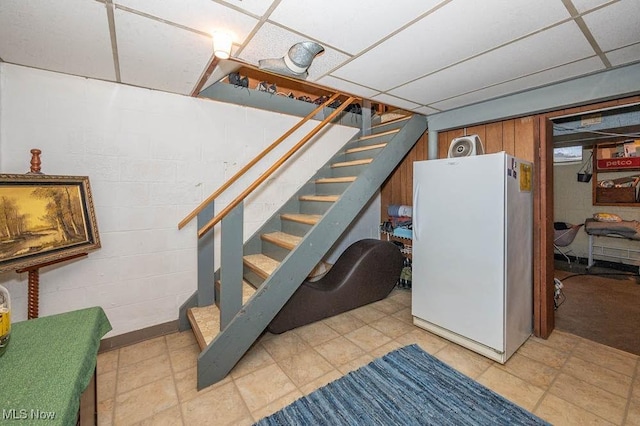 basement with a paneled ceiling and white refrigerator