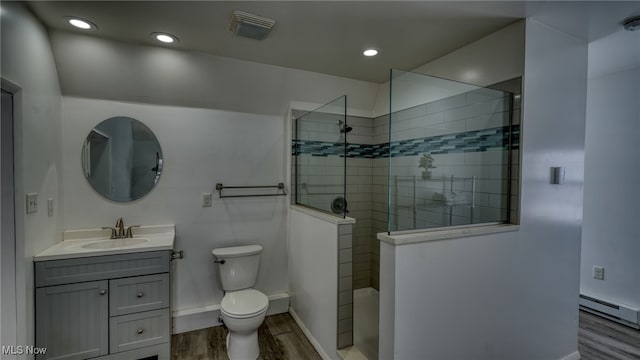 bathroom featuring a tile shower, a baseboard heating unit, hardwood / wood-style floors, toilet, and vanity