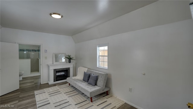 living area with a high end fireplace, hardwood / wood-style floors, and vaulted ceiling