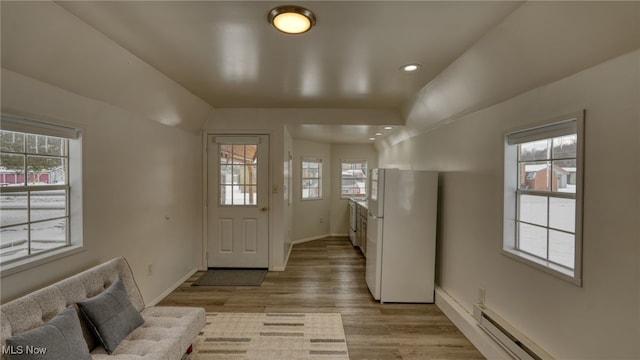 foyer featuring a healthy amount of sunlight, lofted ceiling, light hardwood / wood-style flooring, and a baseboard heating unit