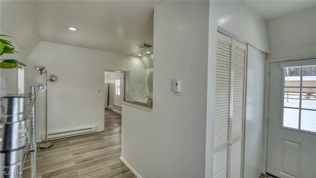 corridor featuring light hardwood / wood-style floors, baseboard heating, and vaulted ceiling