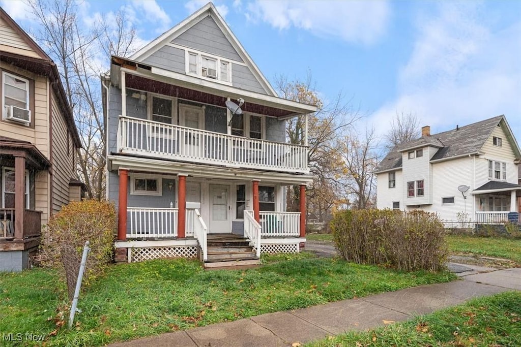 view of front facade featuring covered porch, cooling unit, a balcony, and a front lawn