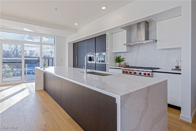 kitchen featuring sink, a center island with sink, white cabinetry, and wall chimney range hood