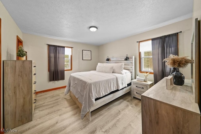 bedroom with a textured ceiling, light hardwood / wood-style flooring, and multiple windows