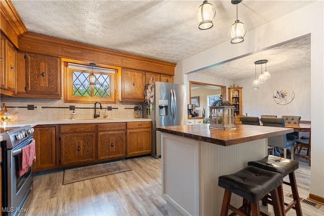 kitchen featuring light wood-type flooring, stainless steel appliances, sink, hanging light fixtures, and a breakfast bar area