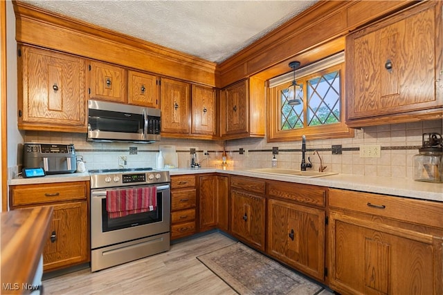 kitchen with appliances with stainless steel finishes, a textured ceiling, sink, decorative light fixtures, and light hardwood / wood-style flooring