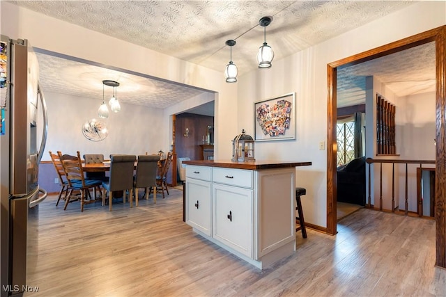 kitchen with a textured ceiling, decorative light fixtures, white cabinets, stainless steel fridge with ice dispenser, and light hardwood / wood-style floors