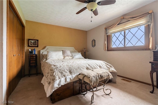 bedroom featuring ceiling fan, a closet, light colored carpet, and a textured ceiling