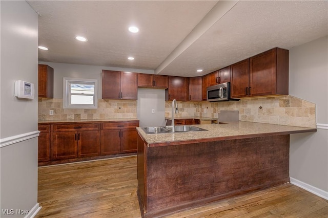 kitchen featuring tasteful backsplash, kitchen peninsula, sink, and light hardwood / wood-style floors