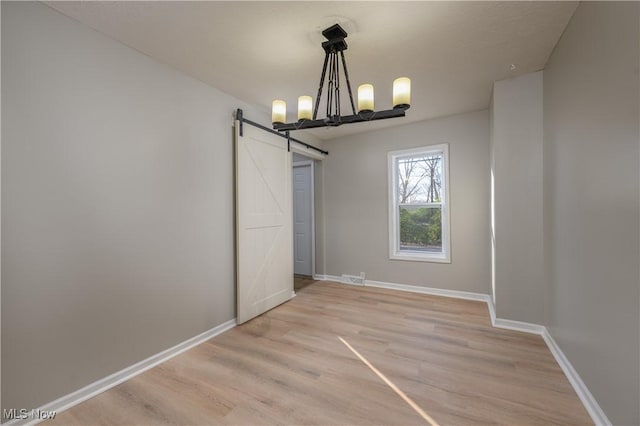 unfurnished dining area featuring light wood-type flooring, a barn door, and a notable chandelier