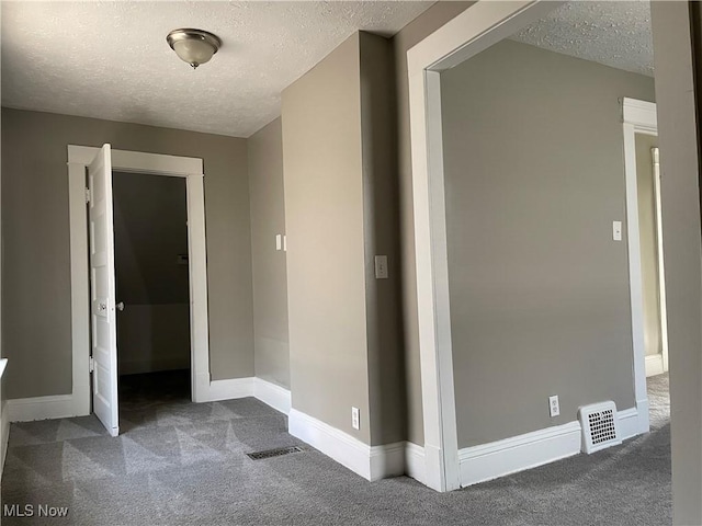 corridor featuring a textured ceiling and dark colored carpet