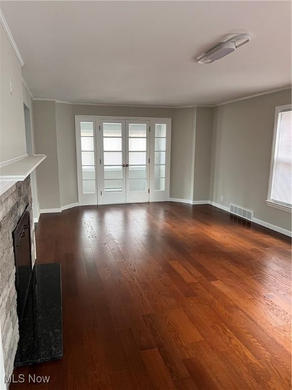 unfurnished living room with a stone fireplace, crown molding, and dark wood-type flooring