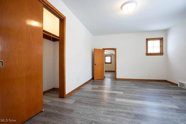 unfurnished bedroom with dark hardwood / wood-style flooring, multiple windows, and a closet