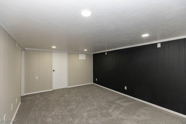 basement featuring carpet flooring, a textured ceiling, and wooden walls