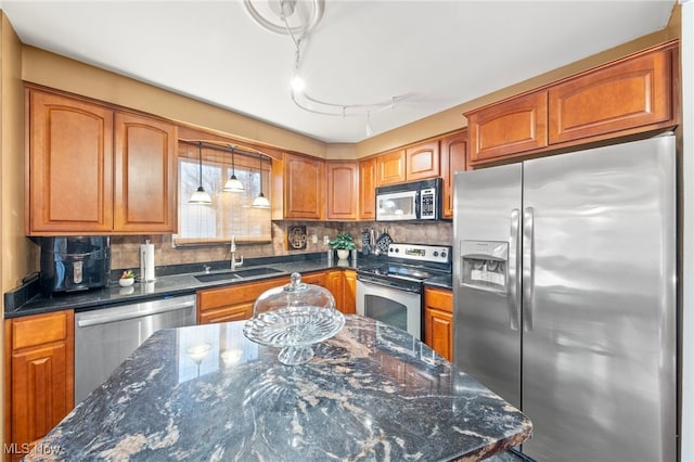 kitchen featuring sink, dark stone countertops, pendant lighting, track lighting, and appliances with stainless steel finishes