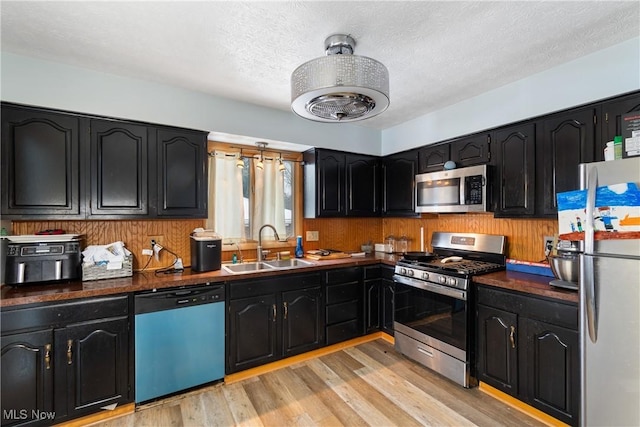 kitchen with appliances with stainless steel finishes, a textured ceiling, light hardwood / wood-style floors, and sink