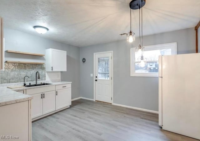 kitchen with pendant lighting, white refrigerator, white cabinetry, and sink