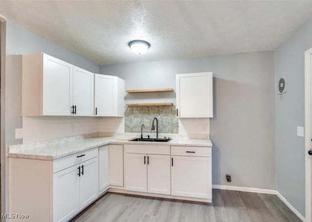 kitchen with white cabinetry, sink, light hardwood / wood-style flooring, a textured ceiling, and decorative backsplash