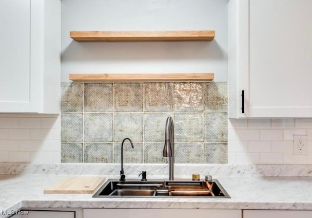 kitchen with tasteful backsplash, light stone counters, sink, and white cabinets