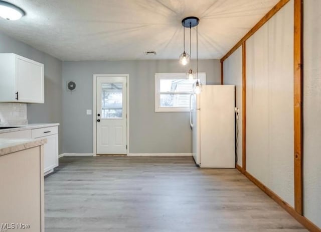 kitchen featuring backsplash, light hardwood / wood-style floors, white cabinets, white fridge, and hanging light fixtures