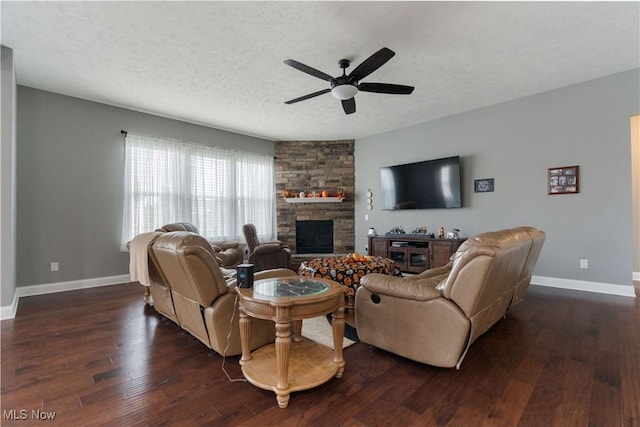 living room with a textured ceiling, a stone fireplace, ceiling fan, and dark wood-type flooring