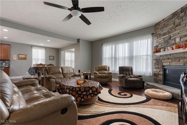 living room with wood-type flooring, a textured ceiling, a stone fireplace, and ceiling fan