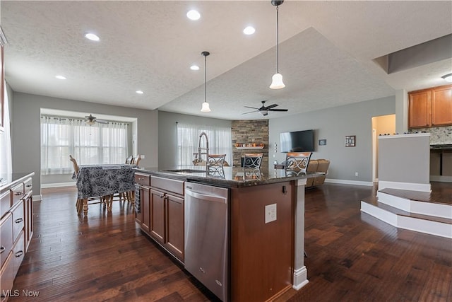 kitchen featuring a center island with sink, hanging light fixtures, stainless steel dishwasher, a textured ceiling, and dark hardwood / wood-style flooring