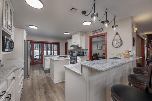 kitchen featuring kitchen peninsula, appliances with stainless steel finishes, white cabinetry, and a kitchen island